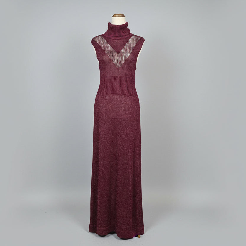 Purple dress on a mannequin against a white wall with a wooden cabinet and framed picture in the background.