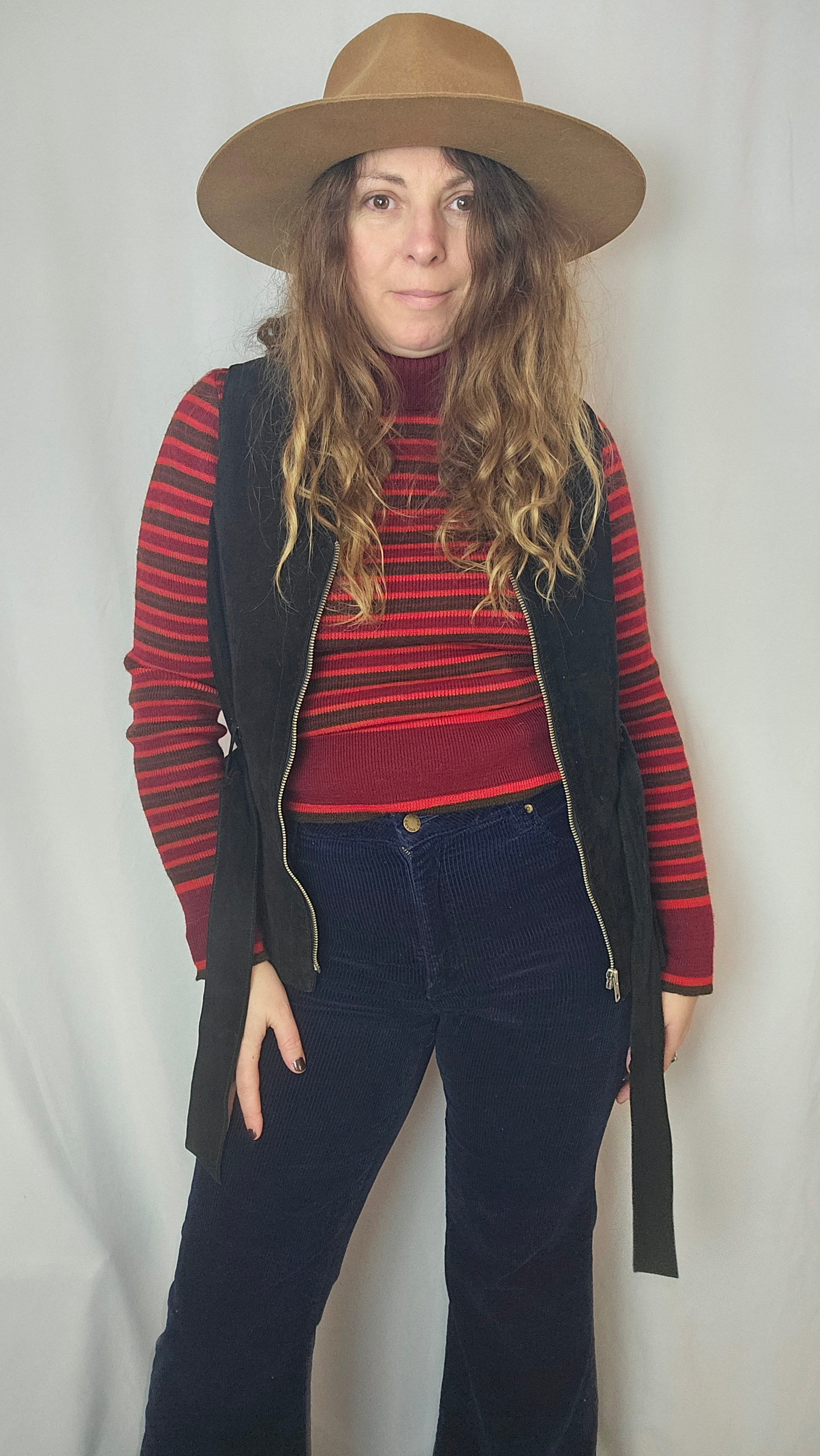 Person wearing a red and black striped sweater with a wide-brimmed hat on a white background