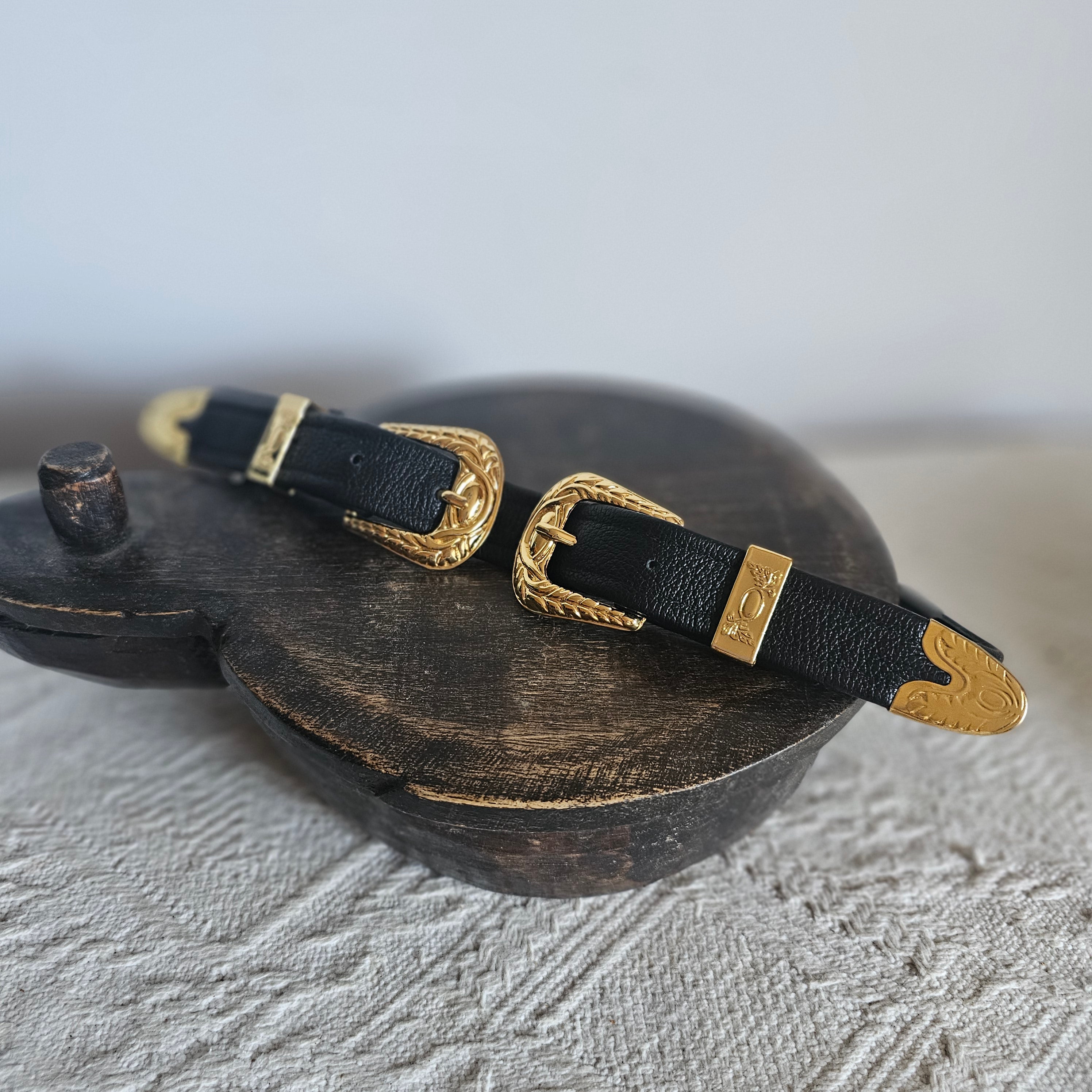 Black leather belt with gold buckles on a textured gray surface