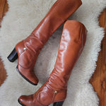 Pair of brown knee-high boots on a white fur rug