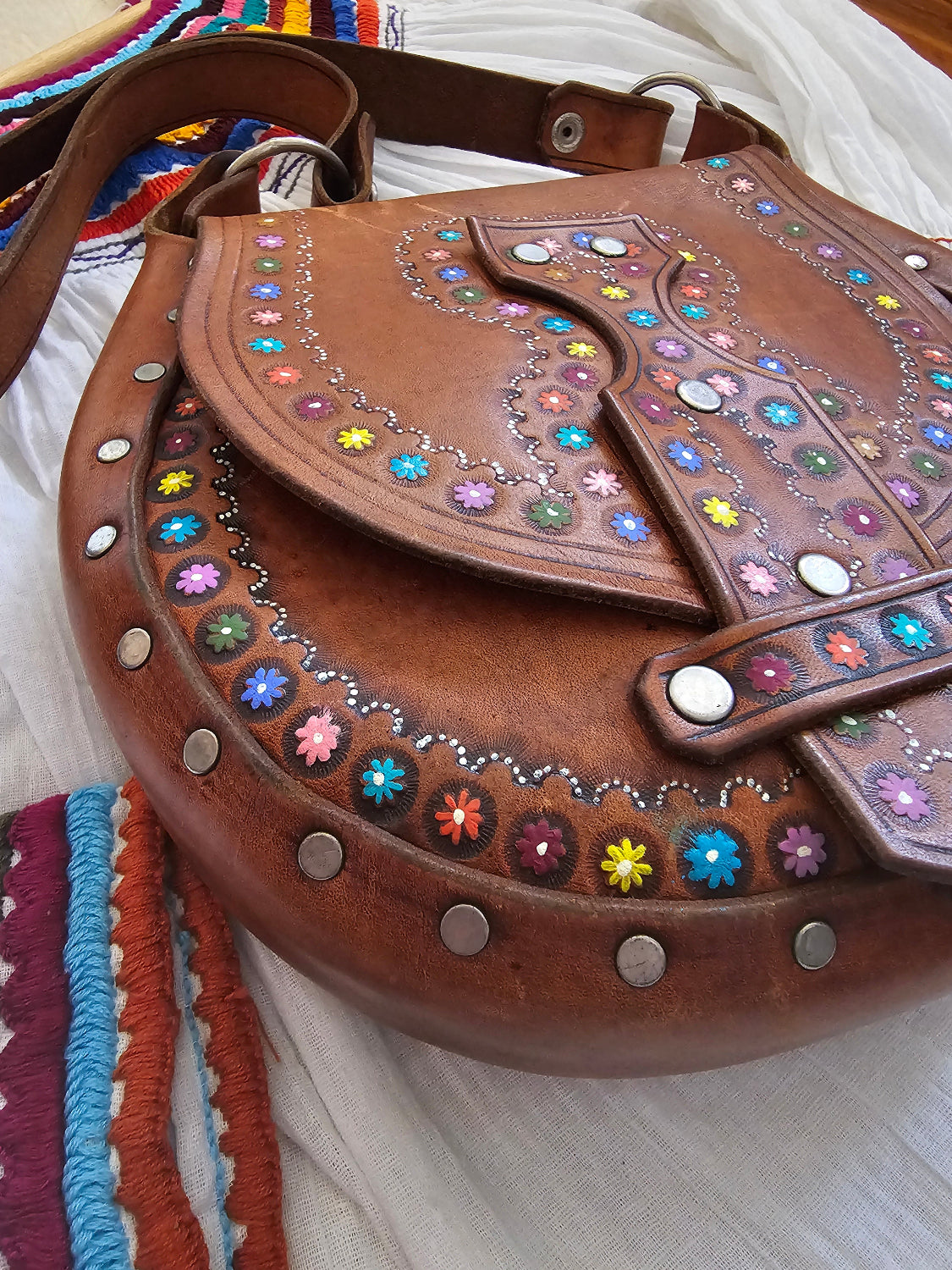 Brown leather bag with colorful gemstones and decorative studs on a white background