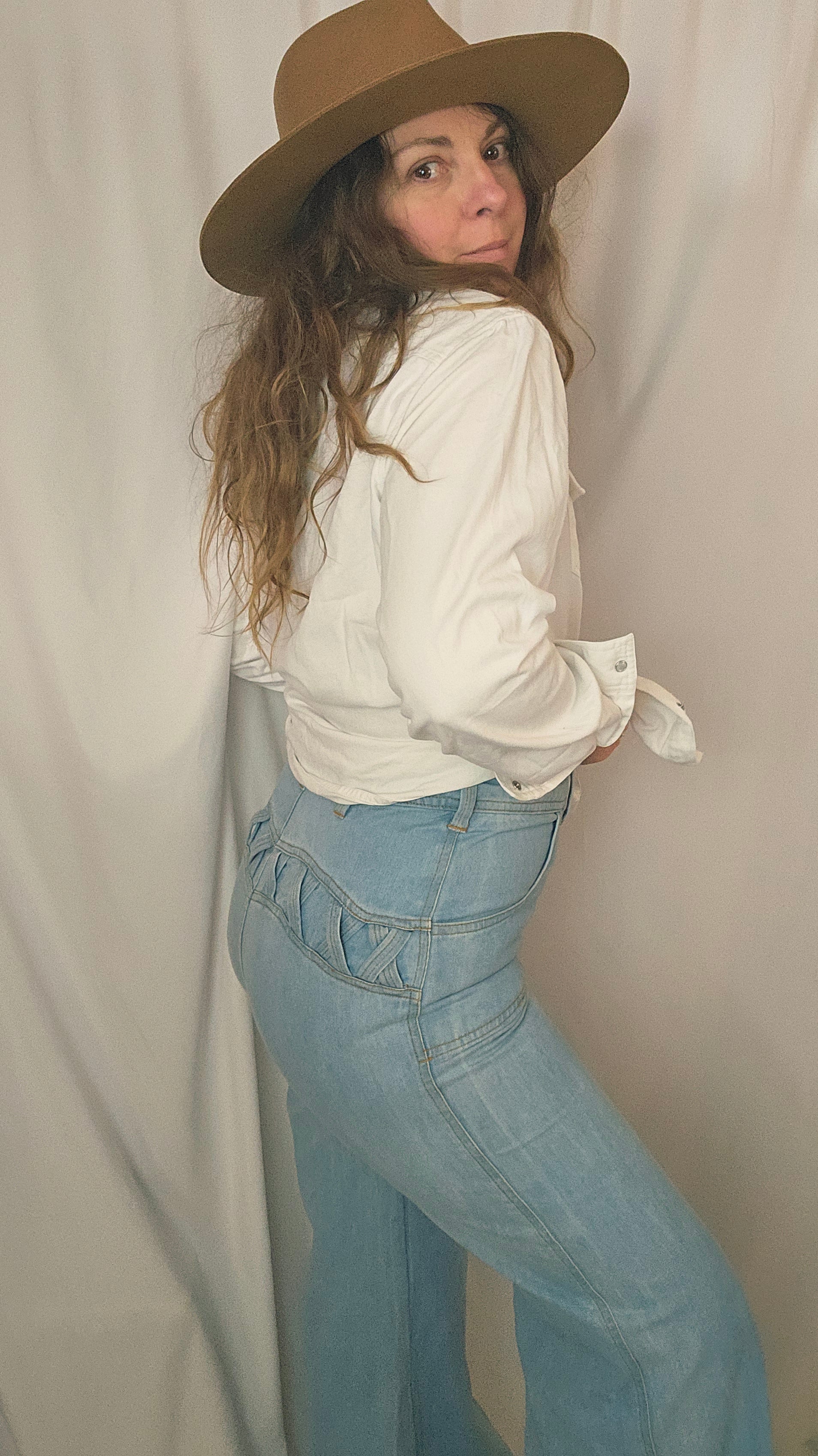 Person wearing a white shirt, blue jeans, and a brown hat lying on a beige surface.