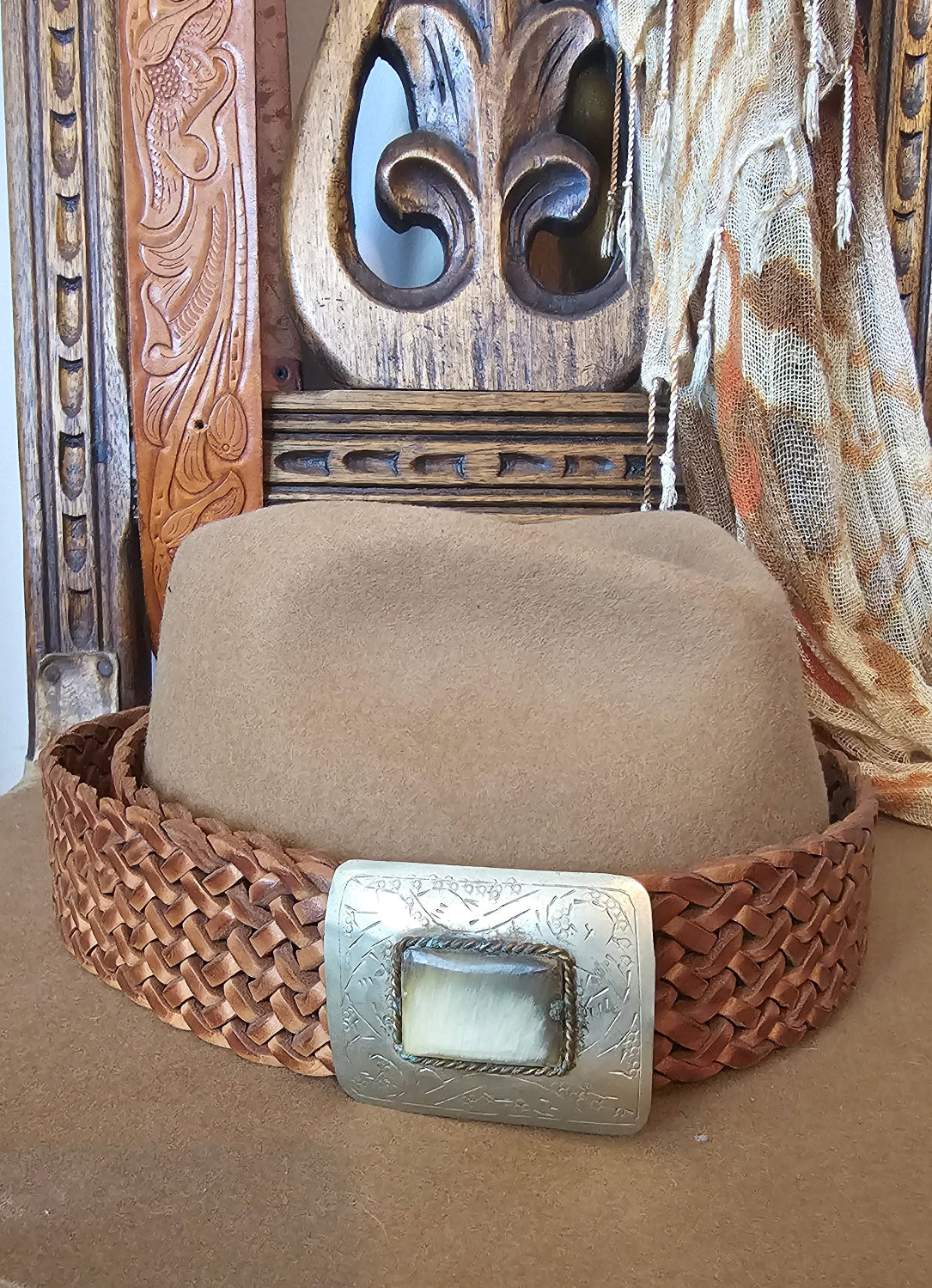 Close-up of a woven leather belt with a metal buckle on a wooden surface.
