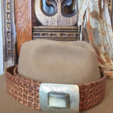 Close-up of a woven leather belt with a metal buckle on a wooden surface.