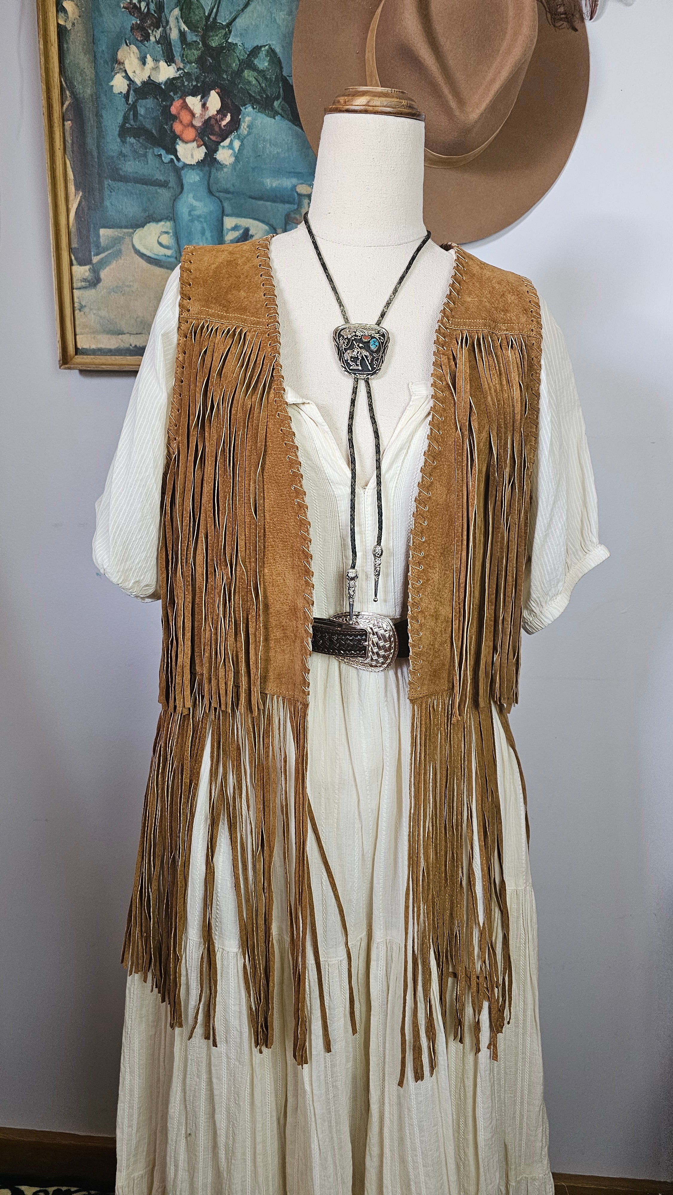 Mannequin wearing a long, fringed garment with a hat against a plain background