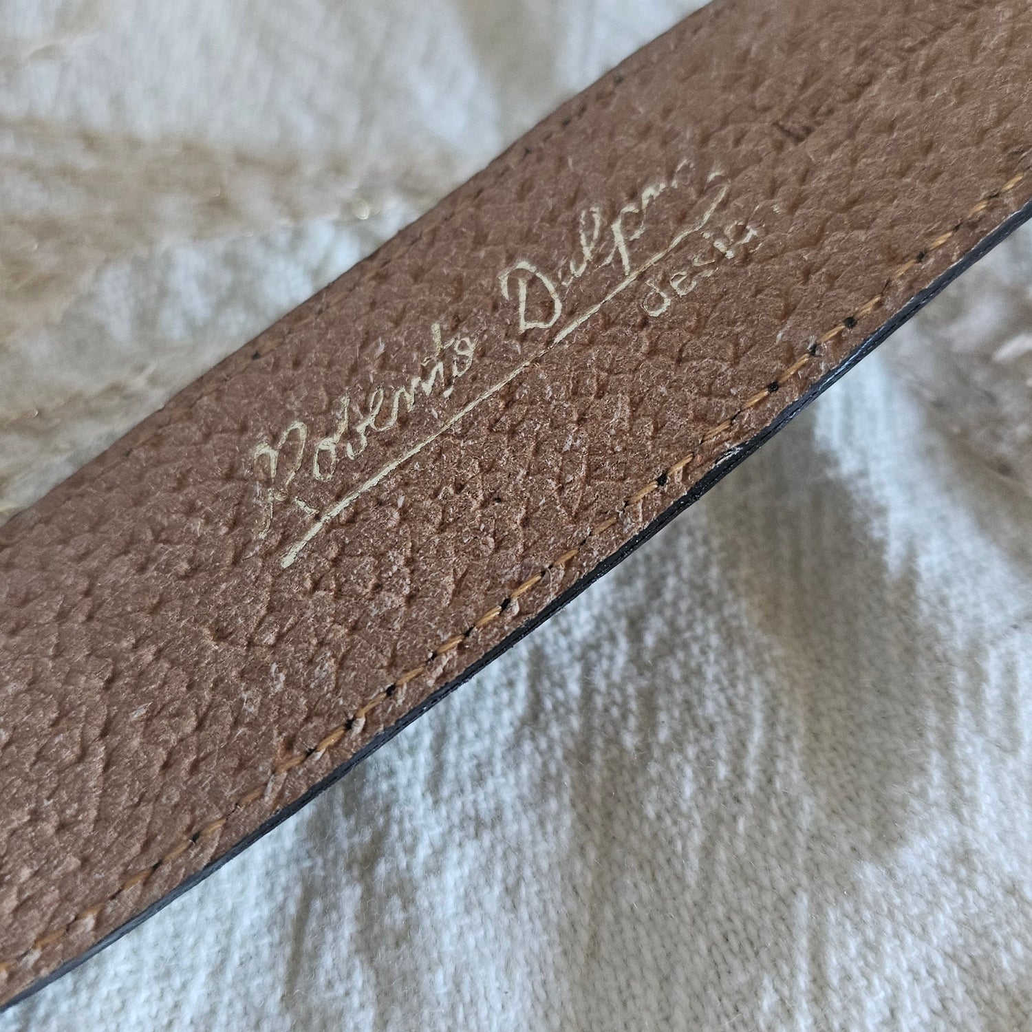 Close-up of a brown leather belt with visible branding on a textured white fabric background