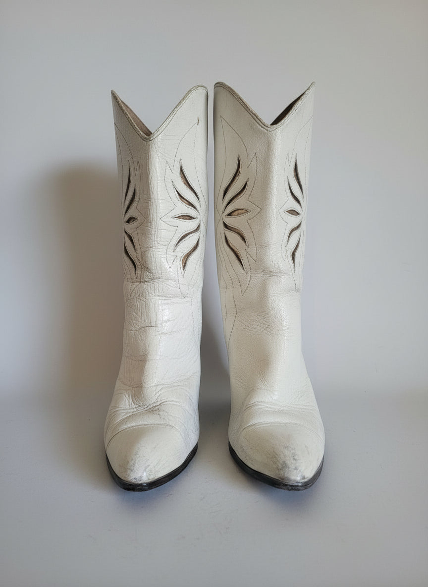 Pair of white cowboy boots with decorative patterns on a light background