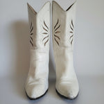 Pair of white cowboy boots with decorative patterns on a light background