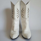 Pair of white cowboy boots with decorative patterns on a light background