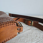 Brown leather bag with strap against a textured light gray wall
