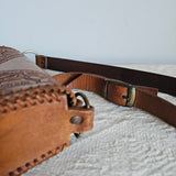 Brown leather bag with strap against a textured light gray wall