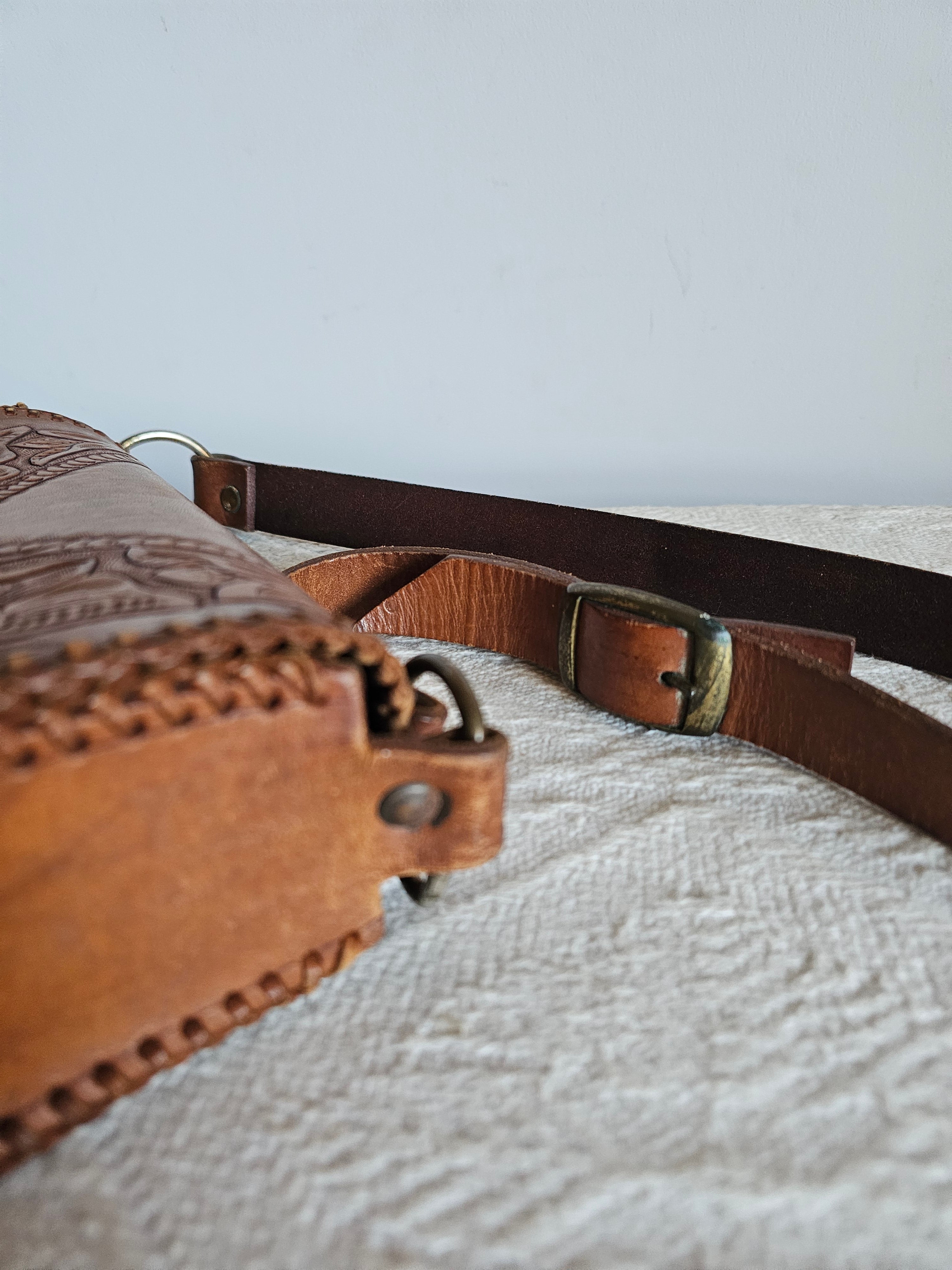 Brown leather bag with strap against a textured light gray wall