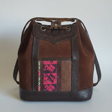 Brown leather bag with embroidered pink design on a textured surface