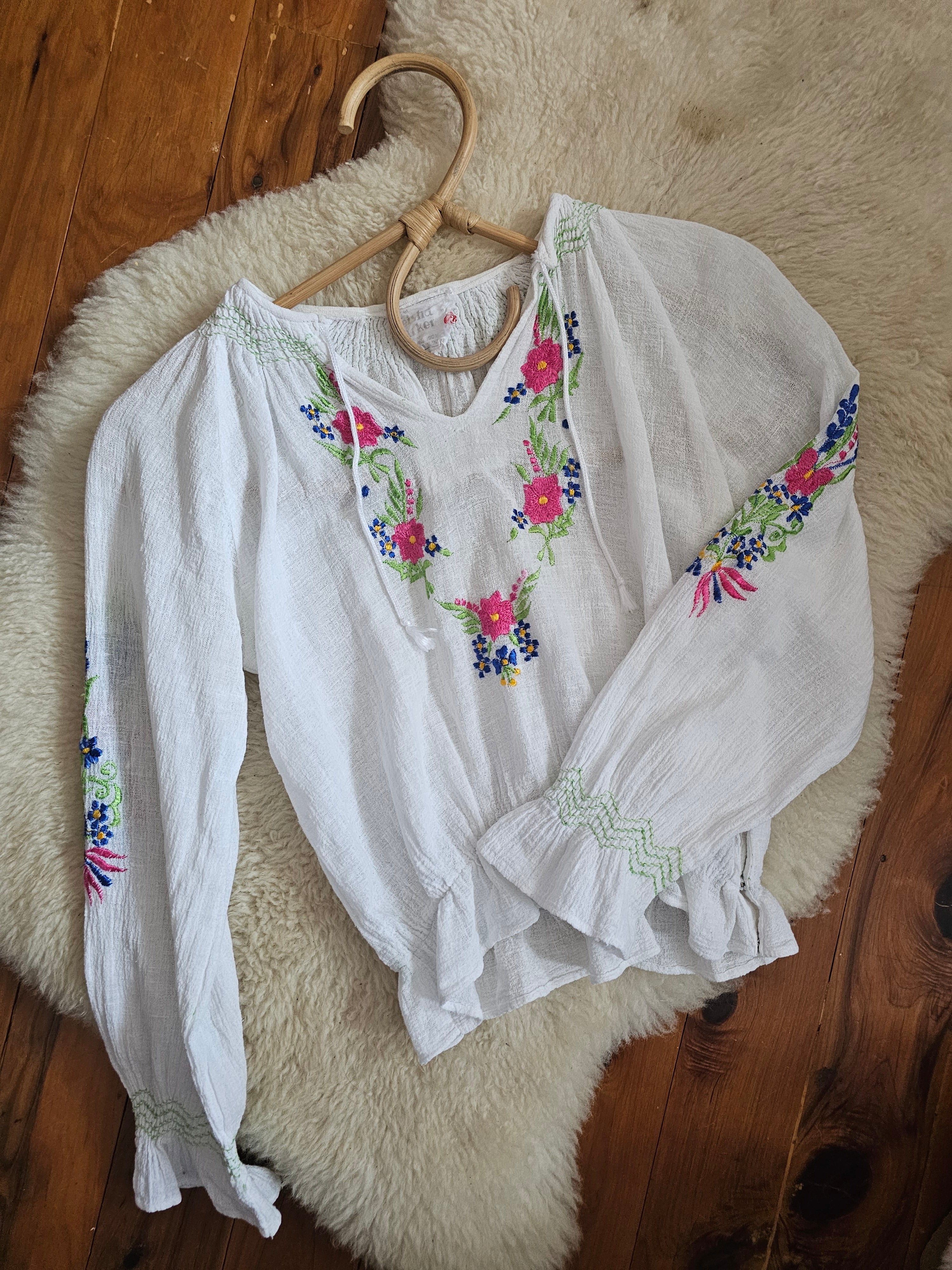 White baby outfit with floral embroidery on a wooden surface