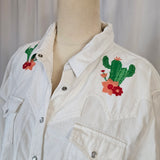 White jacket with embroidered designs on a wooden surface