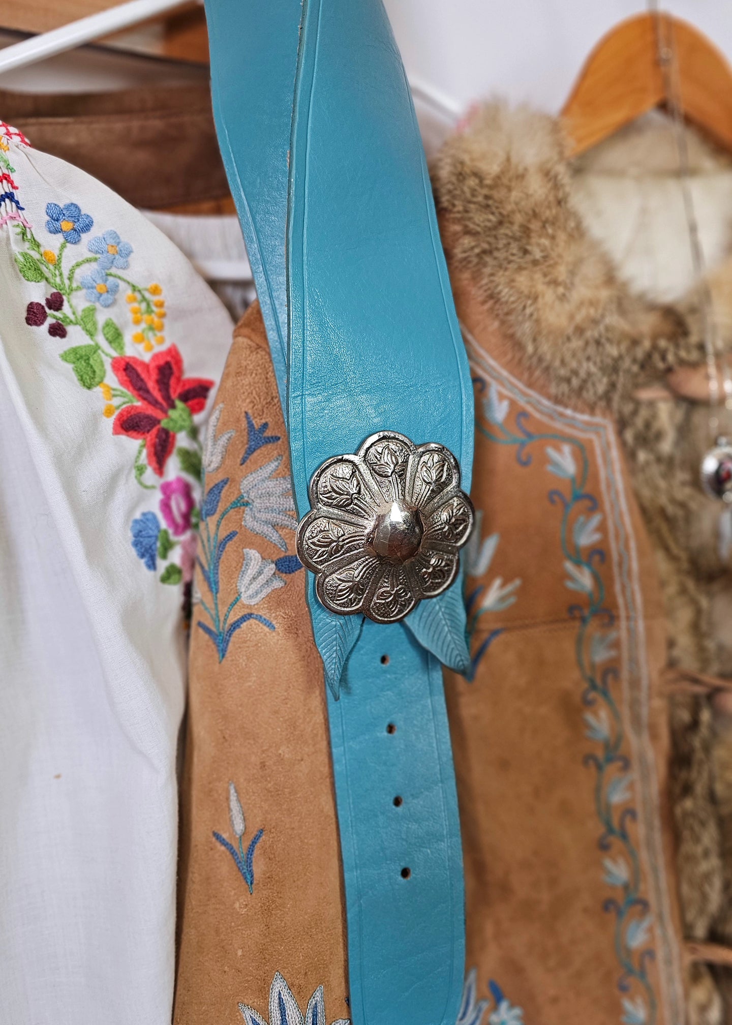 Turquoise leather belt with floral design and metal buckle on a textured surface.