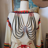 Traditional garment with beadwork on a mannequin against a painting background