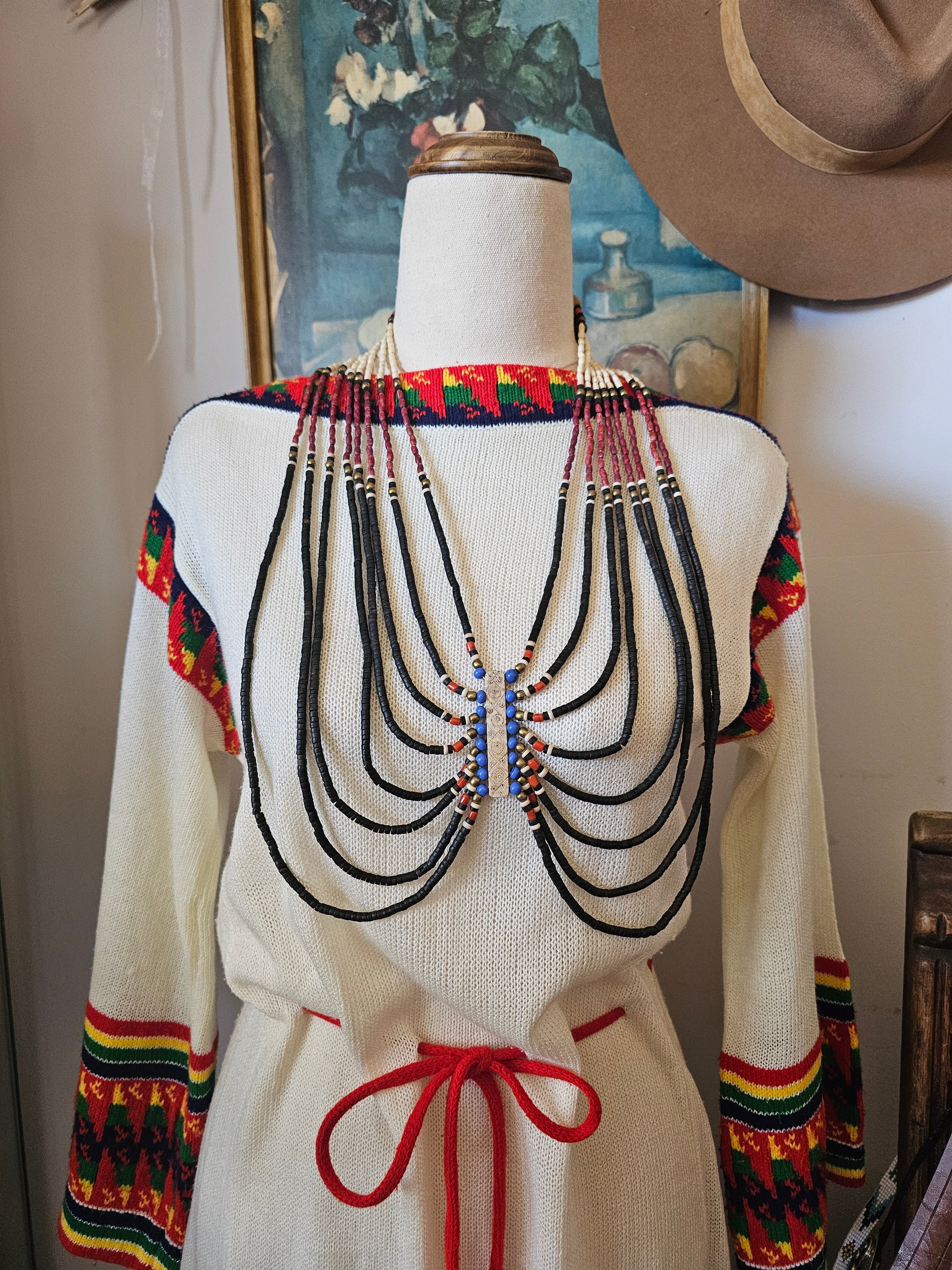 Traditional garment with beadwork on a mannequin against a painting background