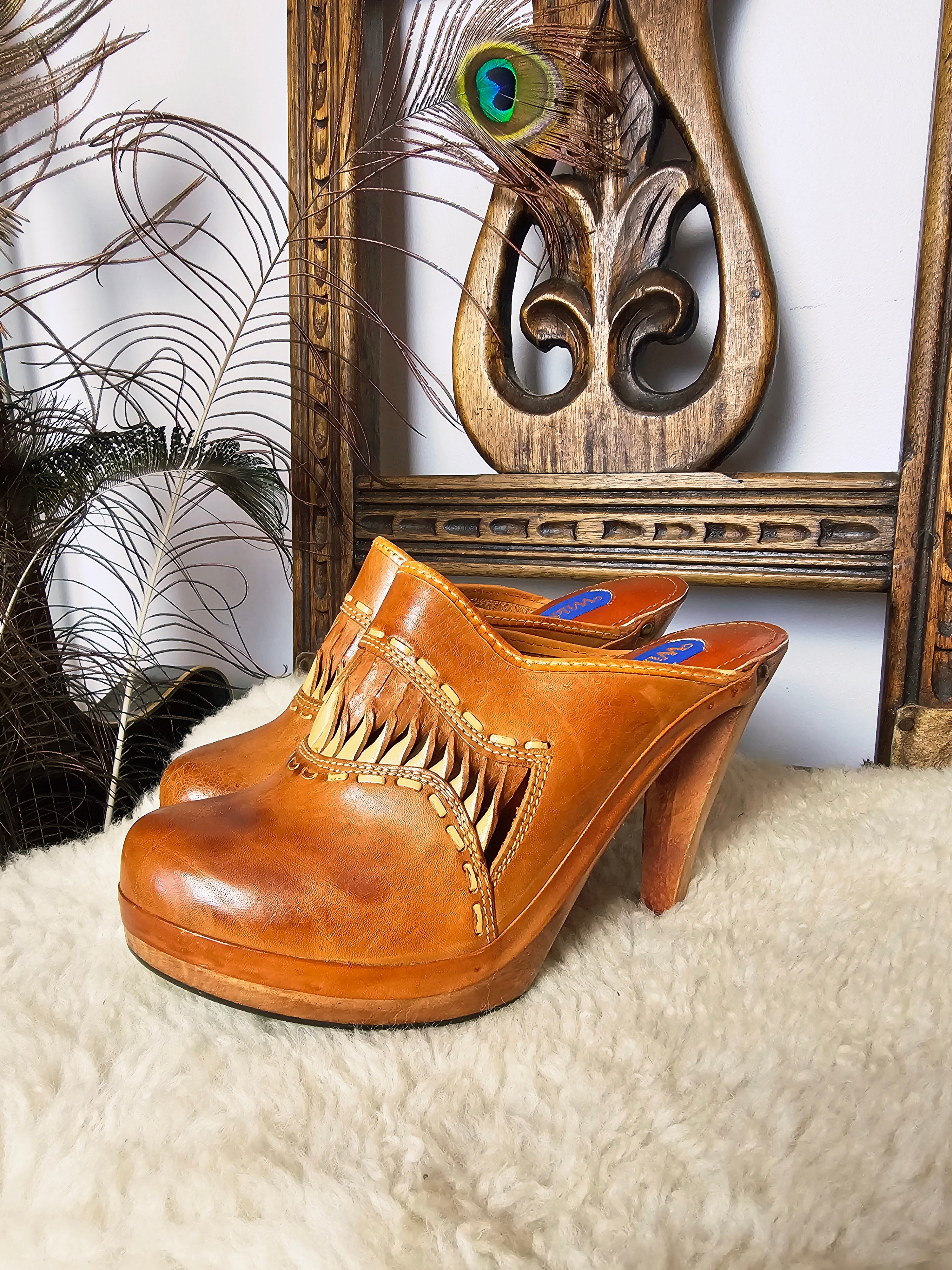 Vintage Wild Pair Tan Leather Mules – Size 37 with carved wood-look heels and fringe detailing, displayed on faux fur with boho decor.