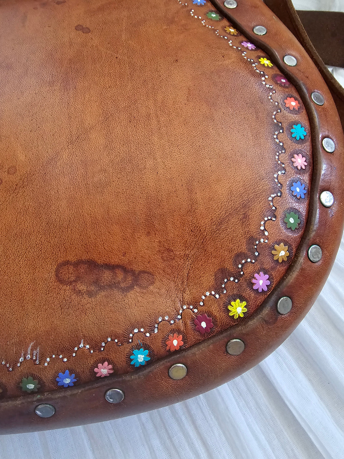 Brown leather saddle with colorful floral patterns and metal studs on a white background
