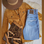 Brown suede jacket, blue jeans, brown boots, and a brown hat on a textured surface.