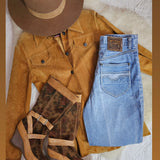 Brown suede jacket, blue jeans, brown boots, and a brown hat on a textured surface.