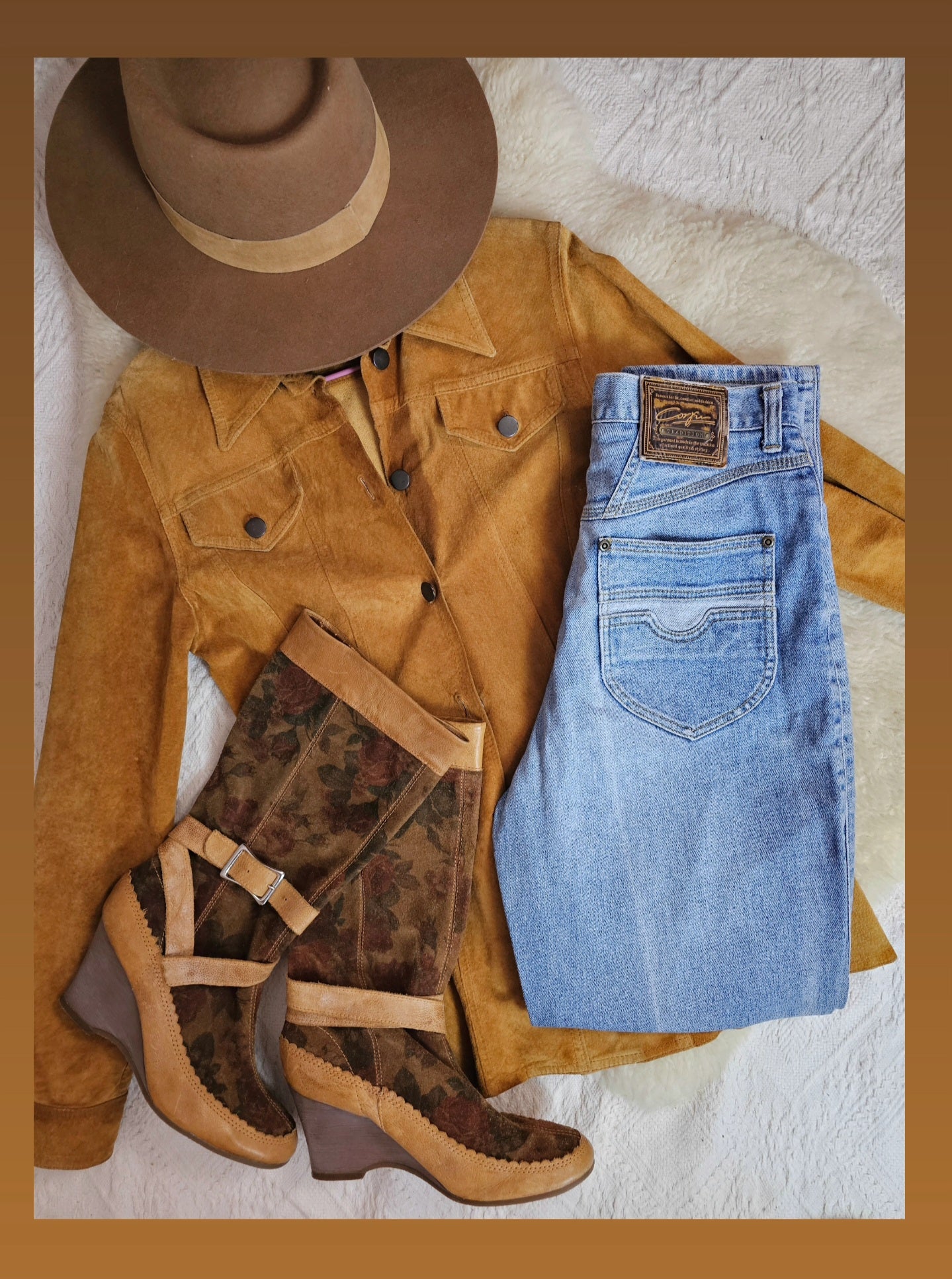 Brown suede jacket, blue jeans, brown boots, and a brown hat on a textured surface.