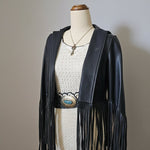 Mannequin wearing a black leather fringe jacket with a white textured garment underneath.
