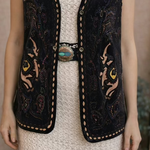 Woman wearing a black embroidered vest over a white dress in a room with a painting on the wall.