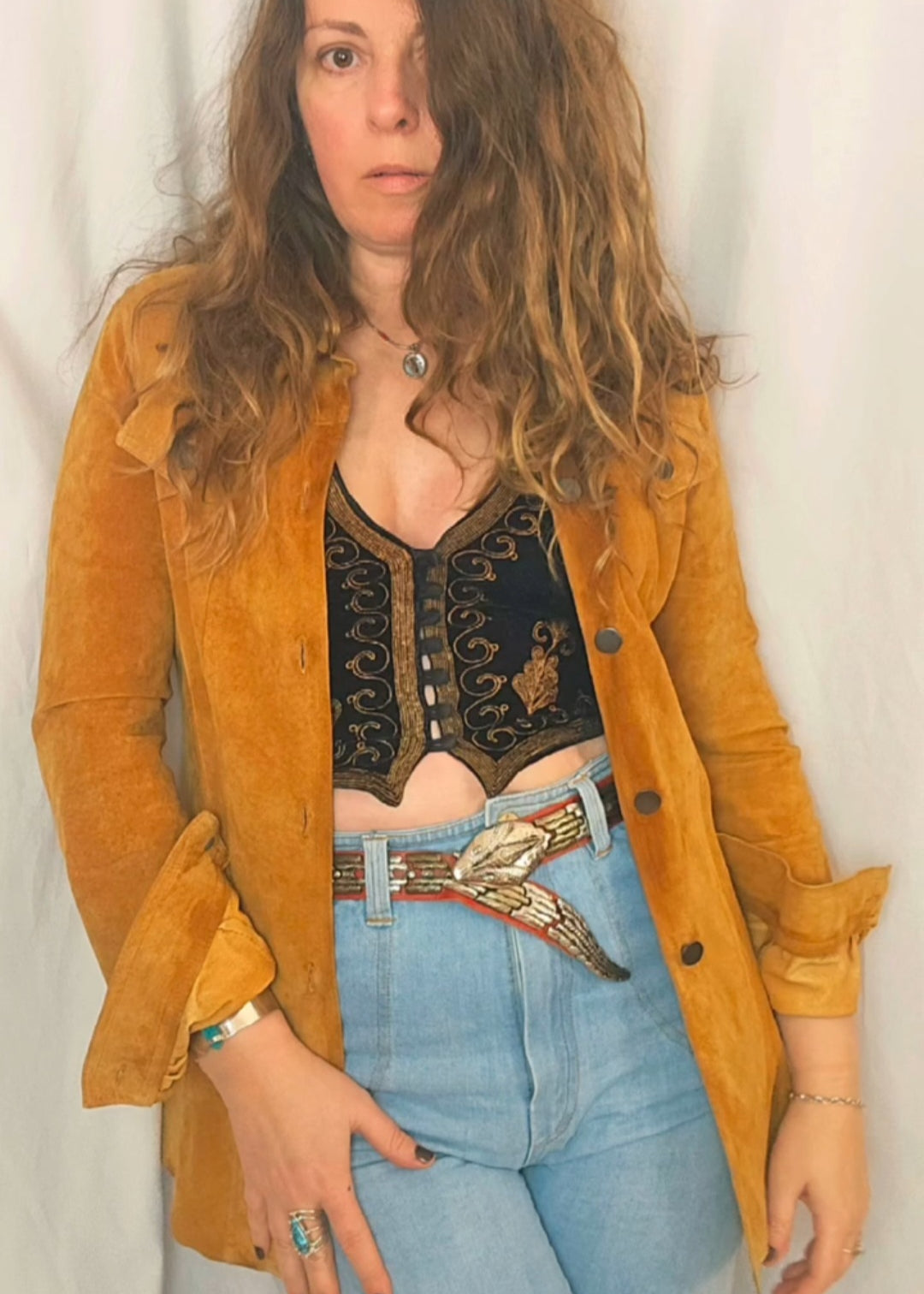 Person wearing a mustard yellow jacket, black top, and light blue jeans with a white background