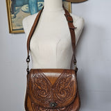 Brown leather handbag with intricate designs on a mannequin against a neutral background
