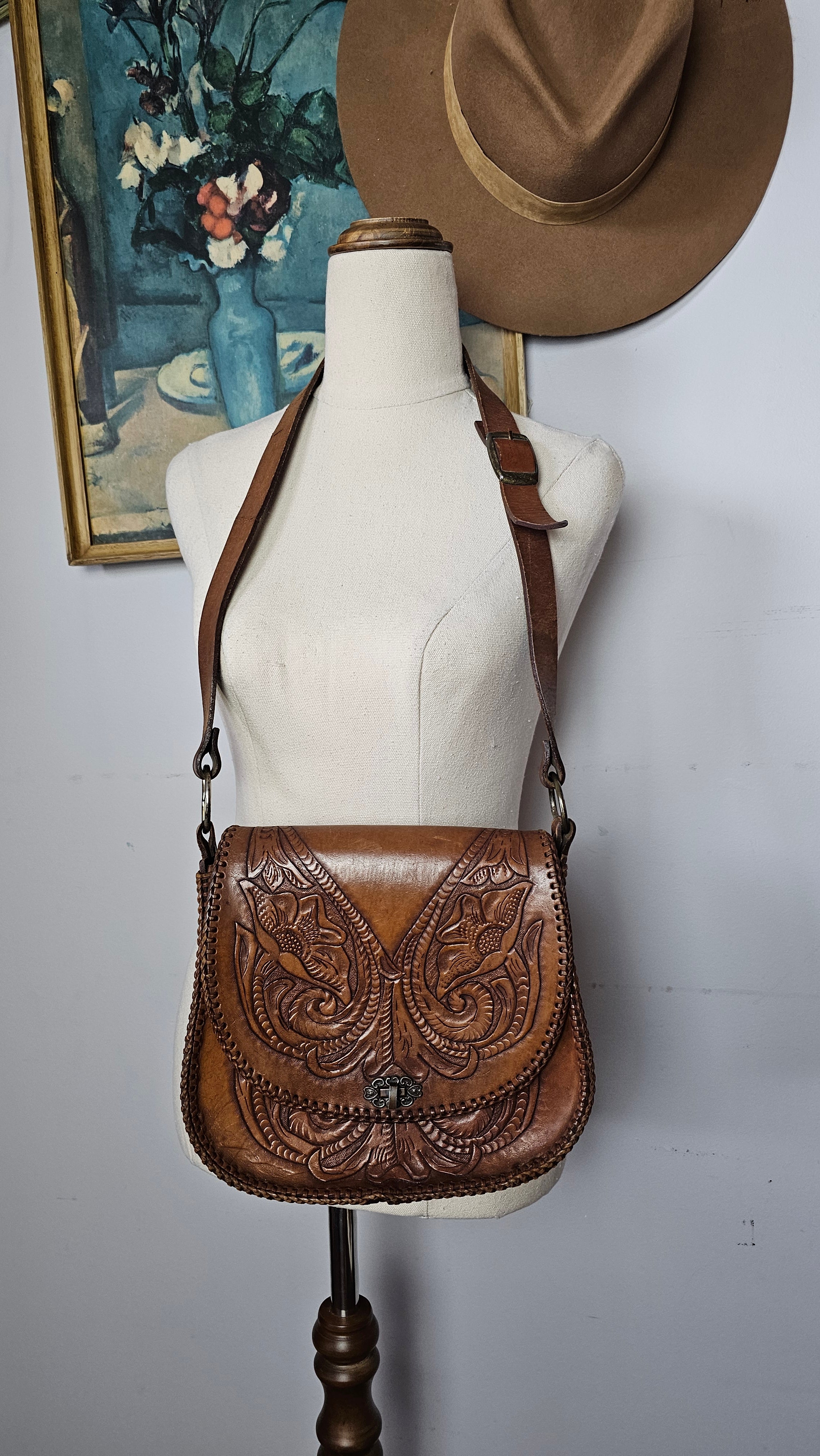 Brown leather handbag with intricate designs on a mannequin against a neutral background