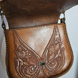 Brown leather bag with intricate embossing on a white background