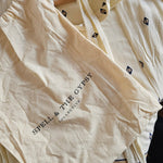 Cream-colored cotton pajama set from Spell & The Gypsy, featuring a long-sleeve top with small black geometric prints and a matching drawstring bag, displayed on a wooden hanger.