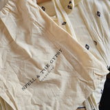 Cream-colored cotton pajama set from Spell & The Gypsy, featuring a long-sleeve top with small black geometric prints and a matching drawstring bag, displayed on a wooden hanger.