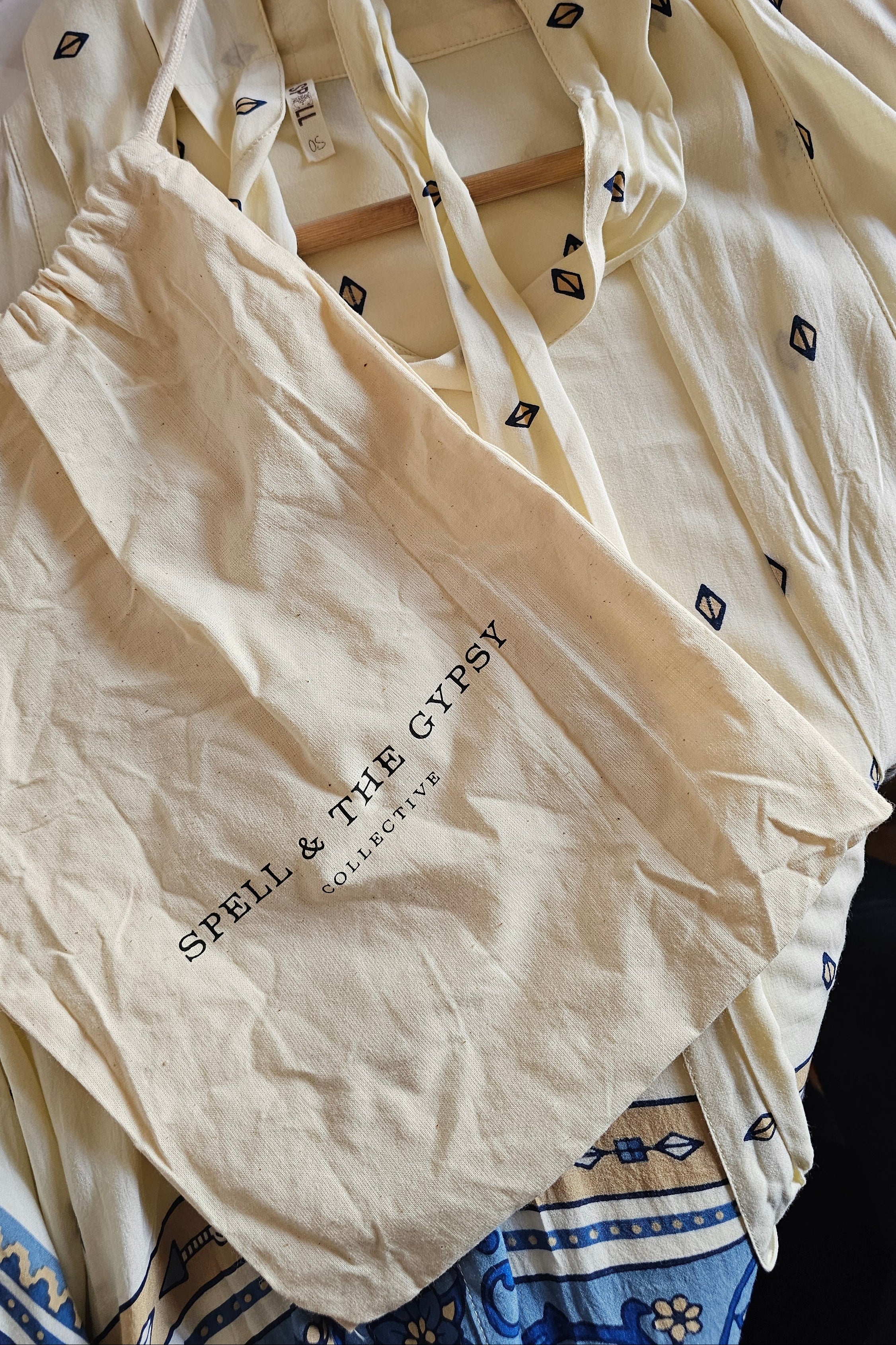 Cream-colored cotton pajama set from Spell & The Gypsy, featuring a long-sleeve top with small black geometric prints and a matching drawstring bag, displayed on a wooden hanger.
