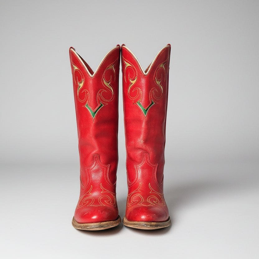 Red cowboy boots with gold patterns on a decorative surface with peacock feathers.
