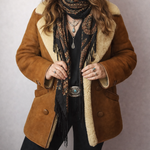 Woman wearing a brown coat with shearling lining, hat, and scarf against a plain background