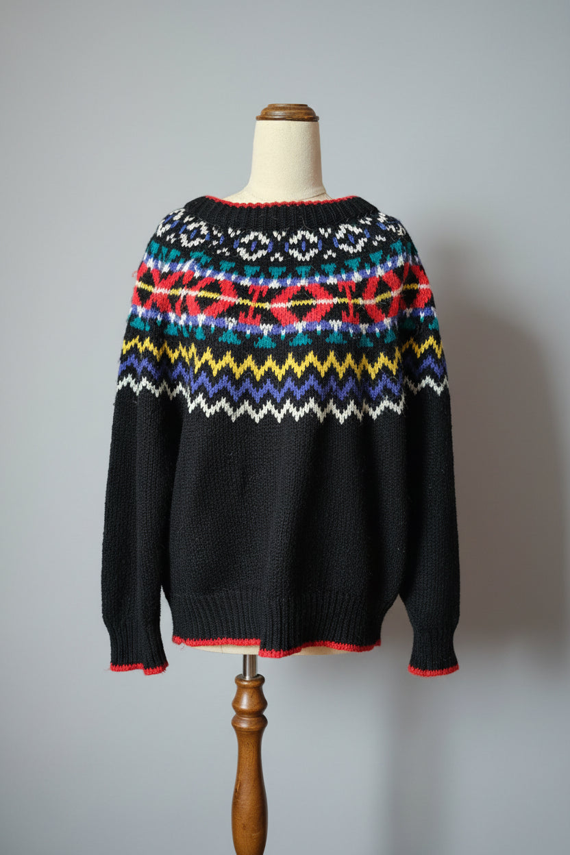Black sweater with colorful pattern on a wooden hanger against a neutral wall.