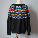 Black sweater with colorful pattern on a wooden hanger against a neutral wall.